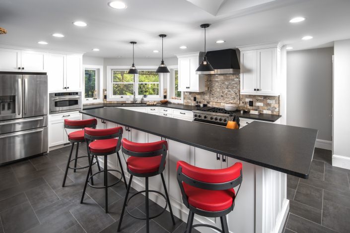white kitchen cabinets with large island and black countertops and dark tile flooring with red bar stools chairs