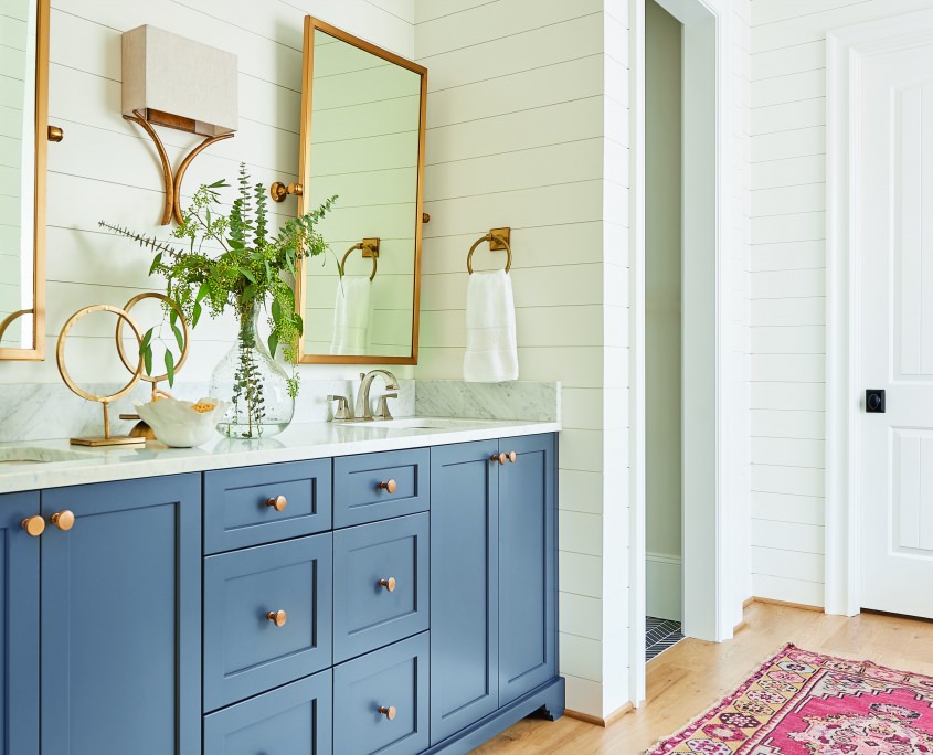 white and blue master bathroom with double sink and white shiplap walls and gold framed mirrors