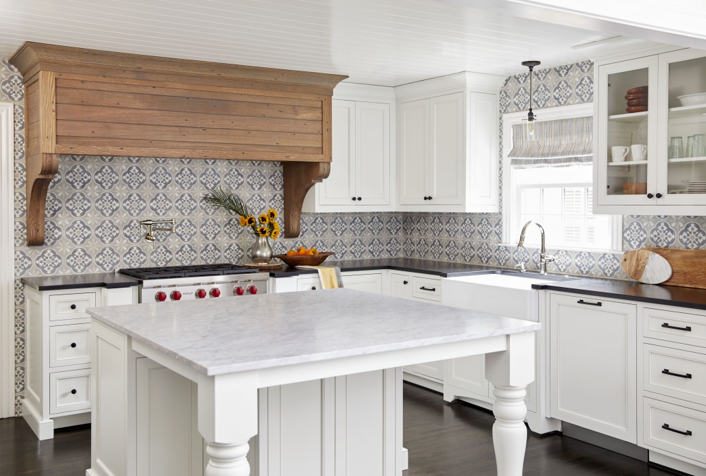 Traditional white kitchen cabinets with kitchen island and white countertops plus a custom wood range hood and black countertops and black hardware